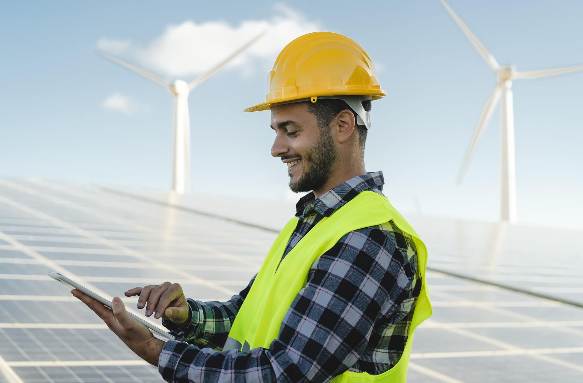 Jeune ingénieur observant sur tablette le plan vert pour l'énergie alternative avec turbine et panneau solaire.